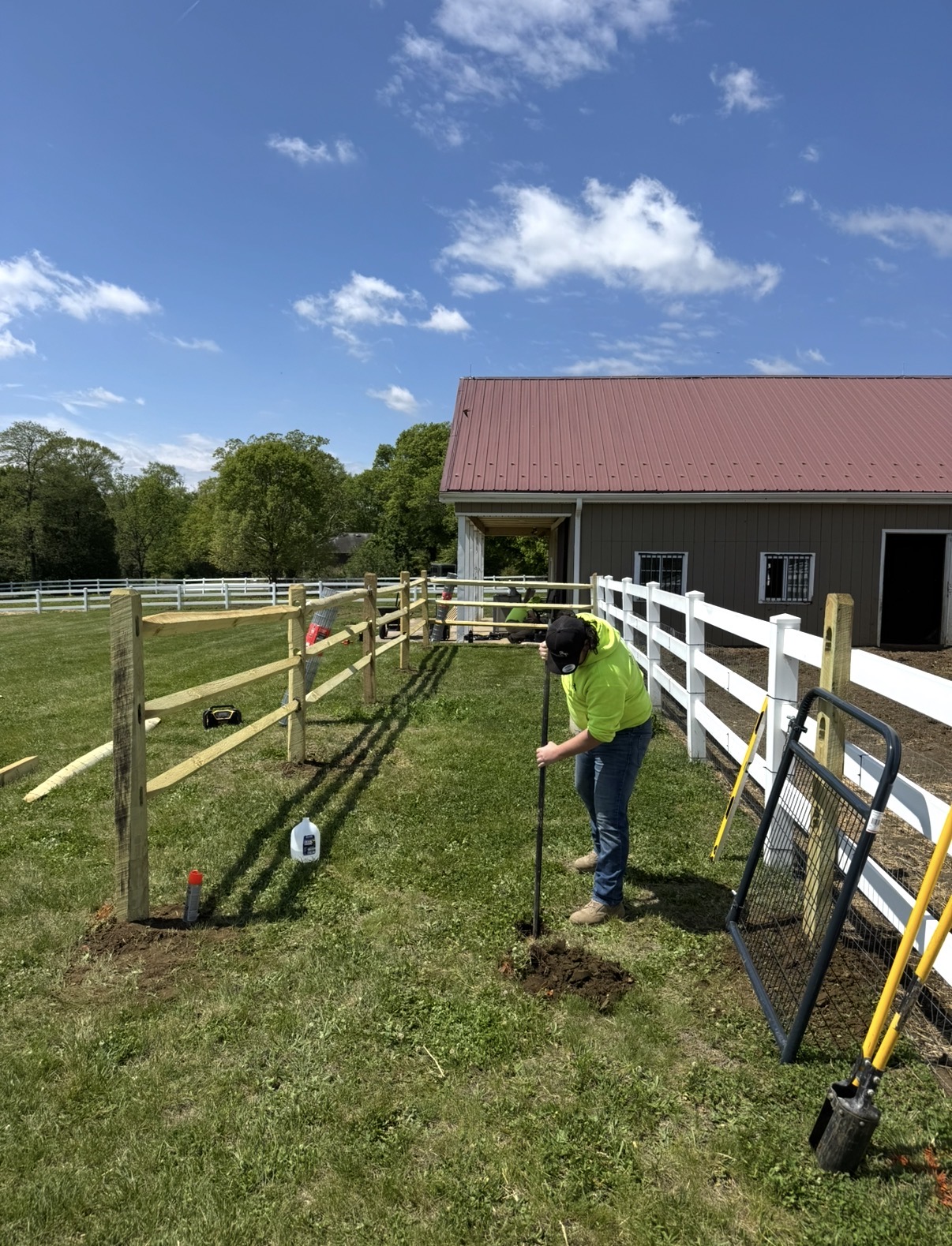 Crew member digging a fence post hole alongside a new split-rail fence